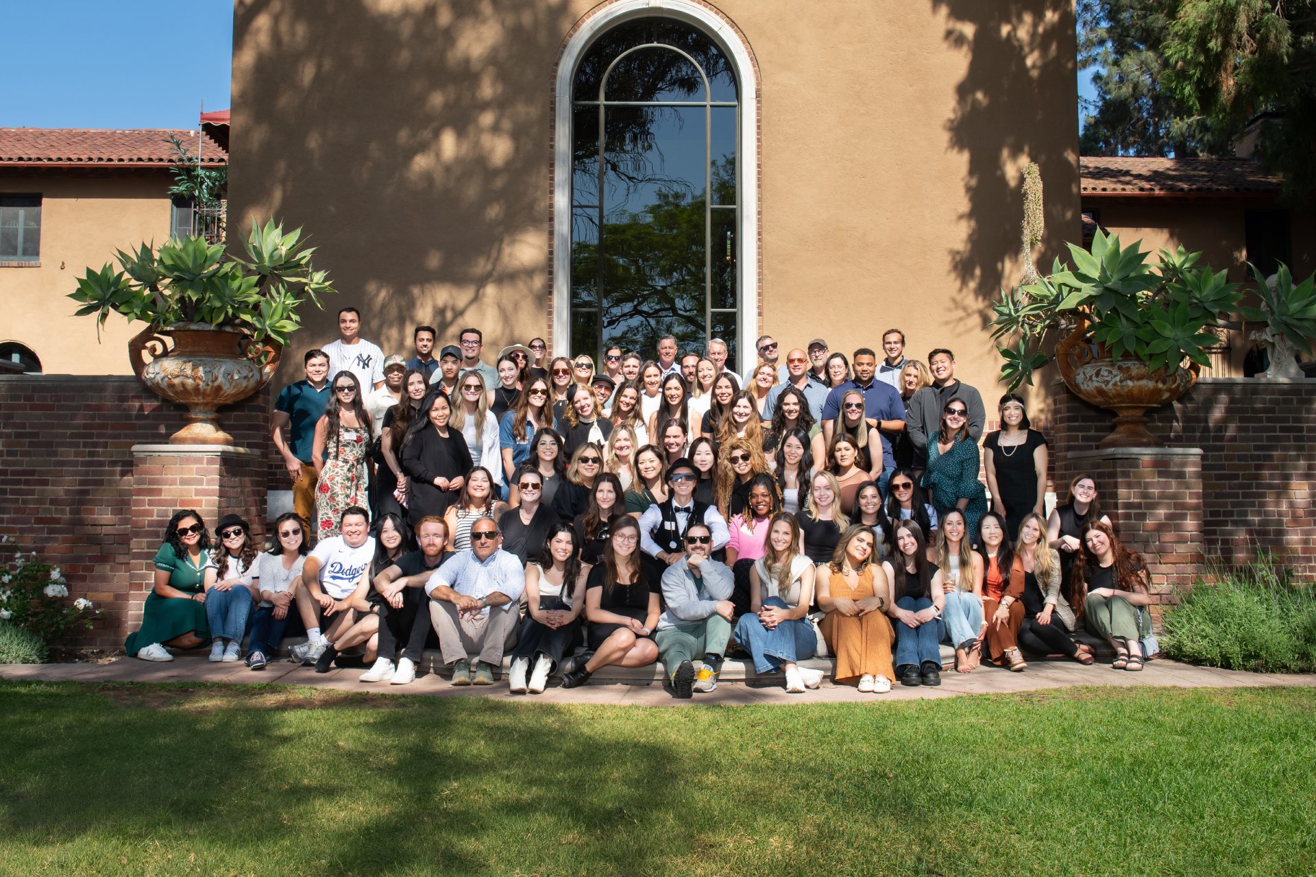 A group of about 75 people pose for a group photo in a shady setting